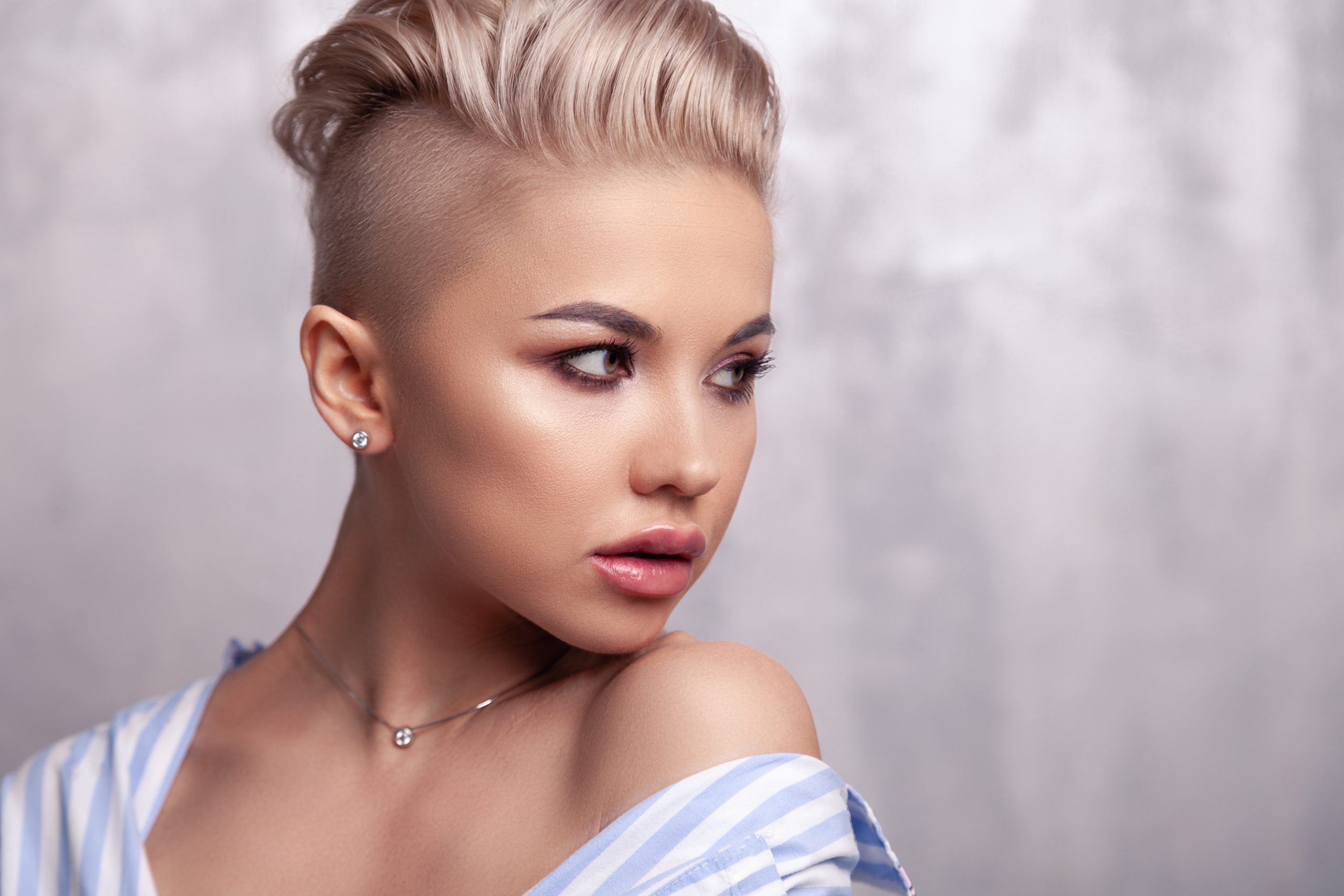 Closeup sexy blonde model with bright make-up, bare shoulders and short hair with shaved temples in modern round silver jewelry earrings, necklace. Сoncept shooting for bijouterie store