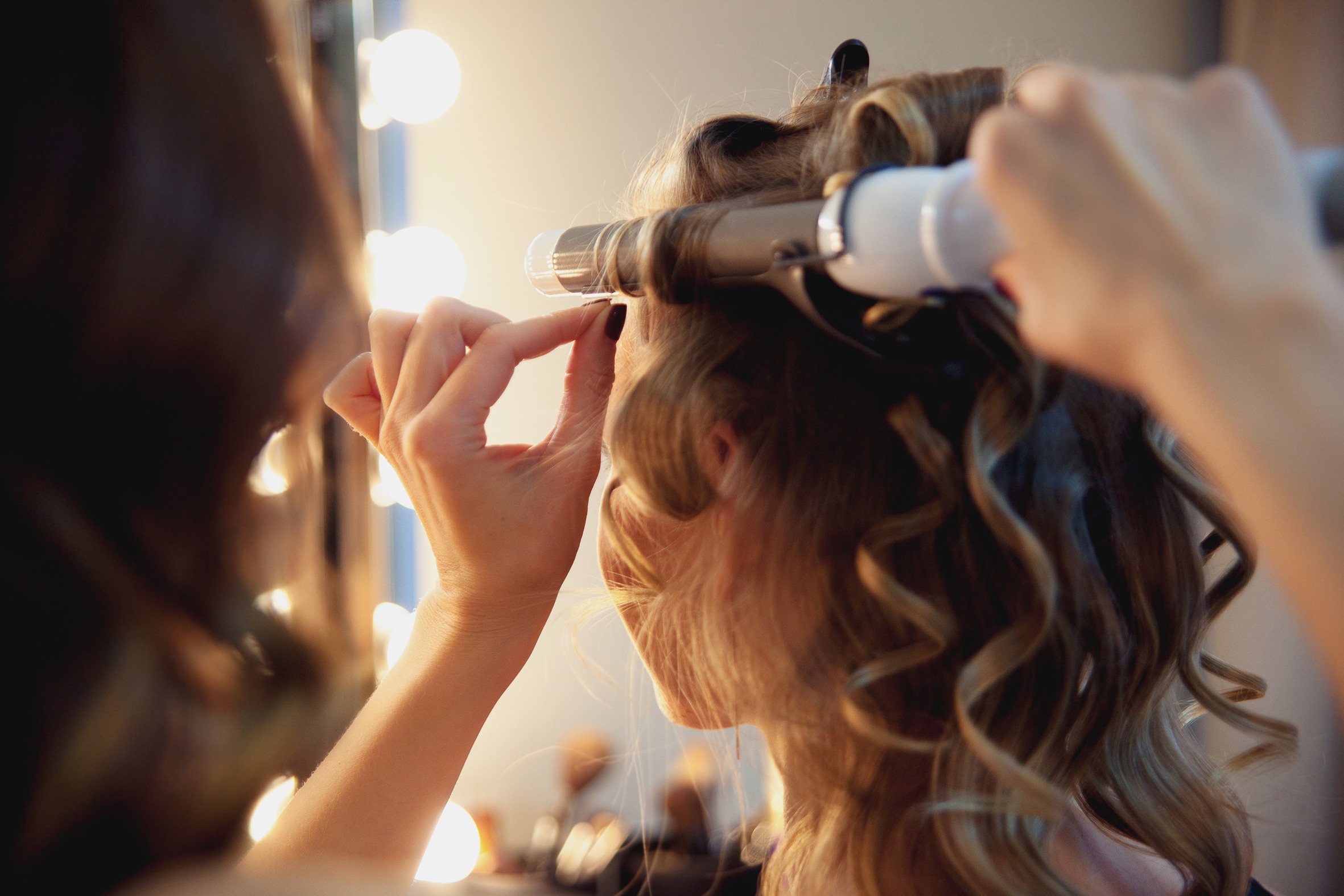 Hairstylist make beautiful curls with curler on light-brown with blonde client's hair. Creating a luxurious evening hairstyle with ringlets of medium length