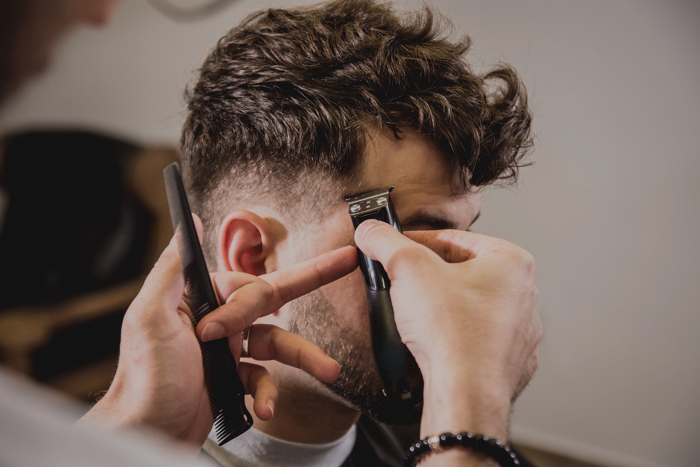 Young man with trendy haircut at barber shop. Barber does the hairstyle and beard trim. Concept barbershop.